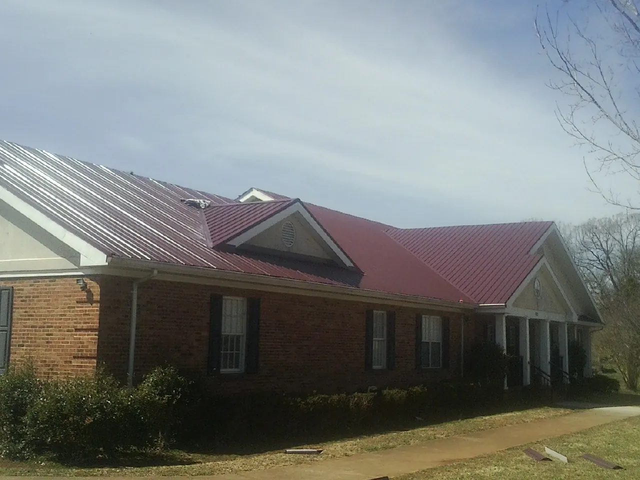 Red metal roof with gabled entries on a long brick building, from a Hail Damage Roof Repair job in Sagamore
