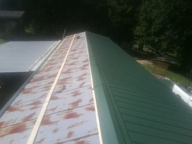 Old rusted panels beside newly installed green metal roofing — Wind Damage Roof Repair by Roofing Brothers in Sagamore