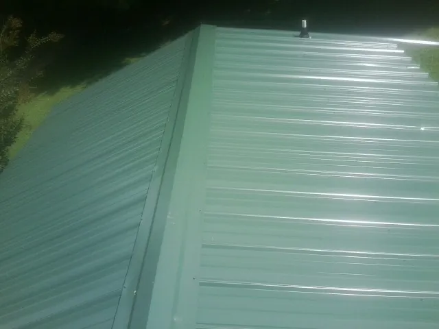 New green metal panels meeting at the ridge of a roof — Flat Roof Repair work by our crew in Sagamore