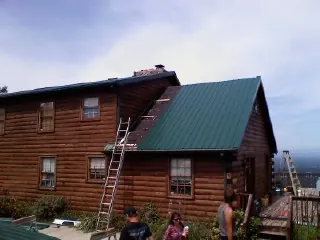 Green metal roof going on a two story log home with ladders set in Sagamore