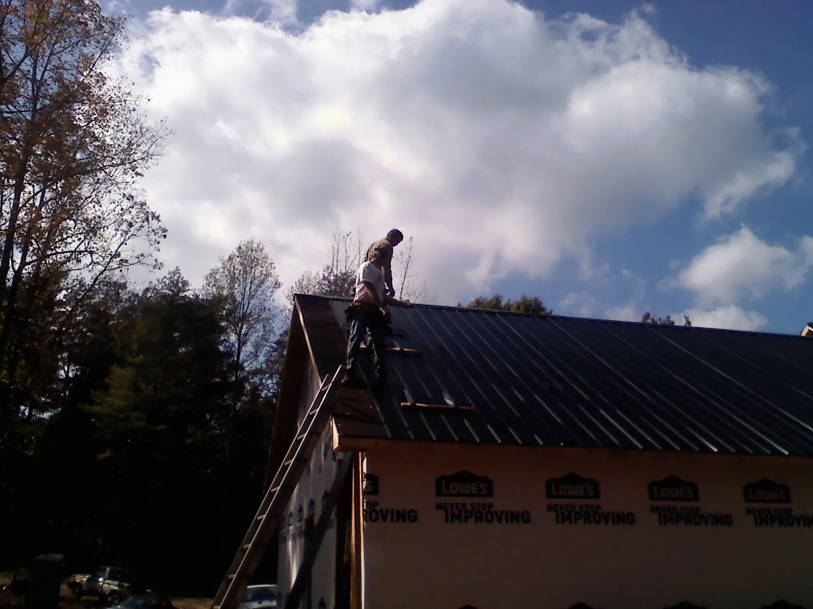 Roofer fastening dark metal panels high against a cloudy sky, from a Roof Inspection job in Sagamore