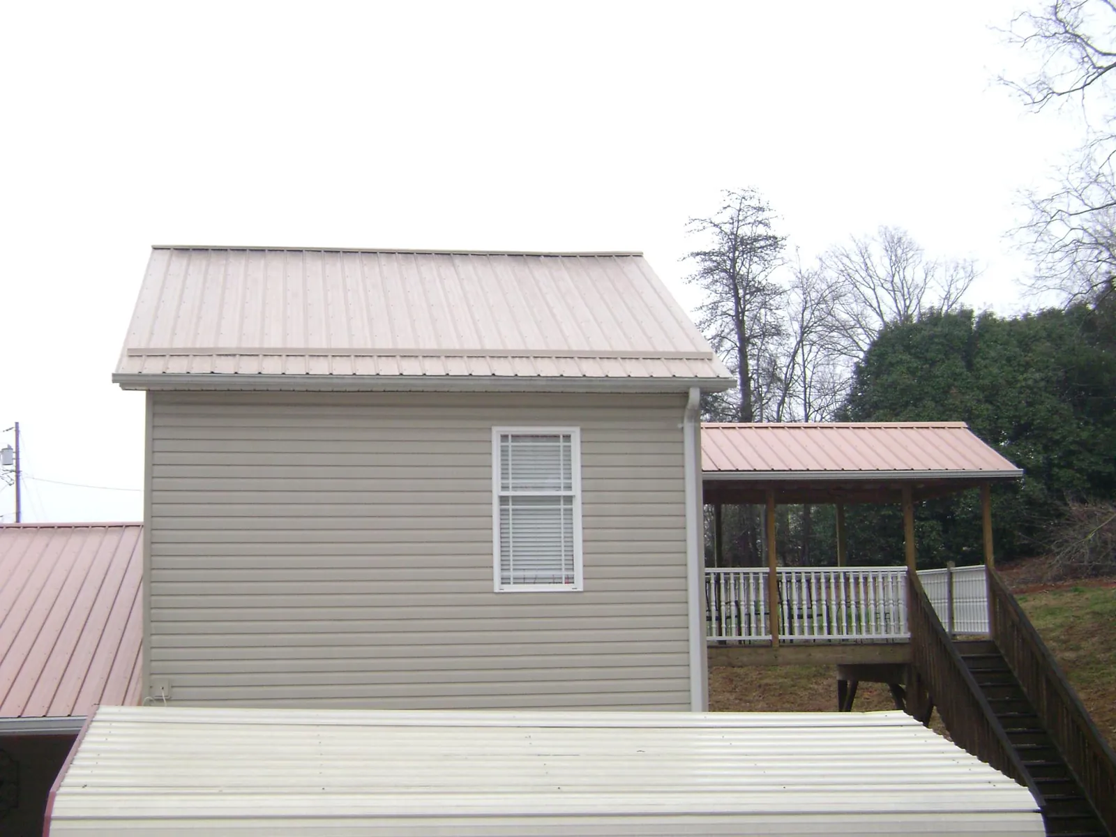 Tan metal roofs on a two story addition and attached porch, from a Roof Replacement job in Sagamore